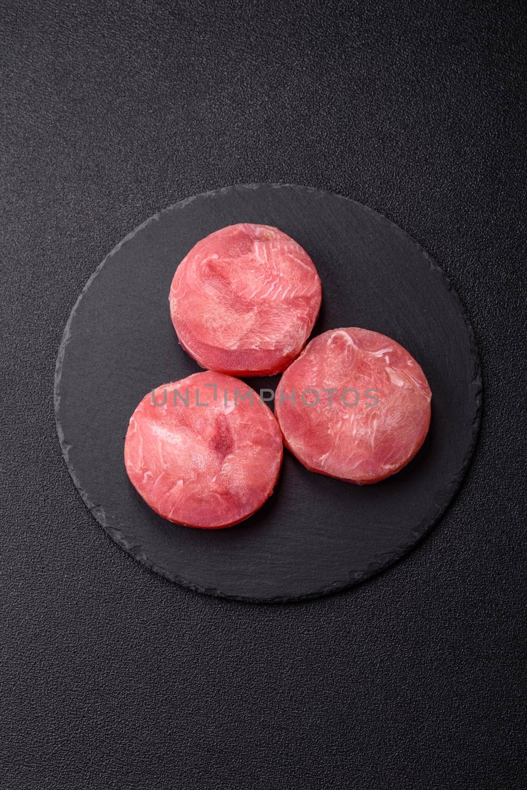 Two fresh slices of raw tuna fillet with spices and herbs on a dark concrete background