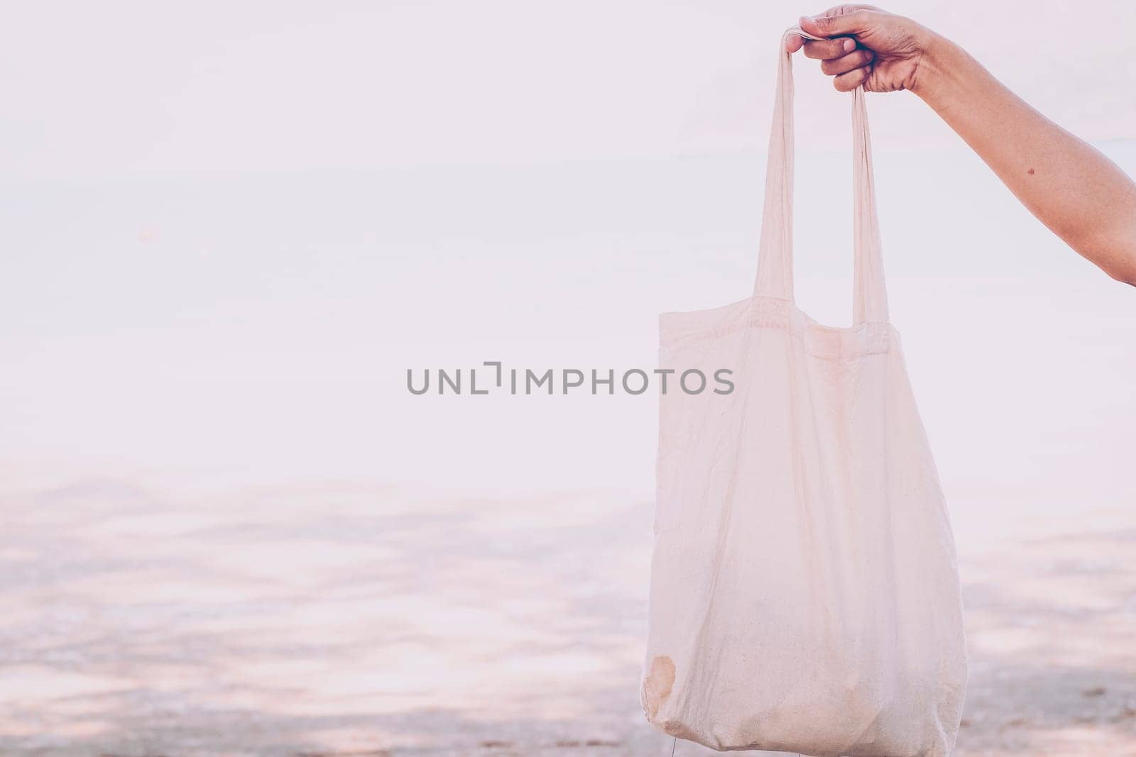 White blank cotton eco tote. Design mockup. Holding blank canvas tote bag, design mockup. Handmade shopping tote bag for girls. Beach background. Summer idea