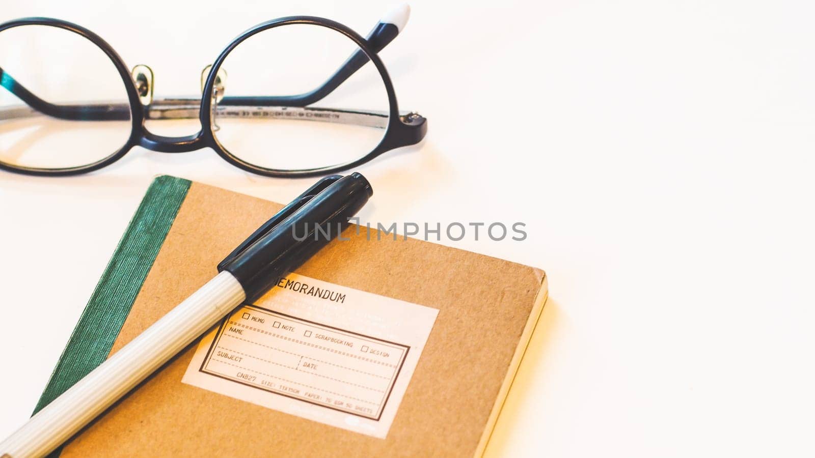 Brown craft paper cover notebook with pen and eyeglasses on desk isolated white background.
