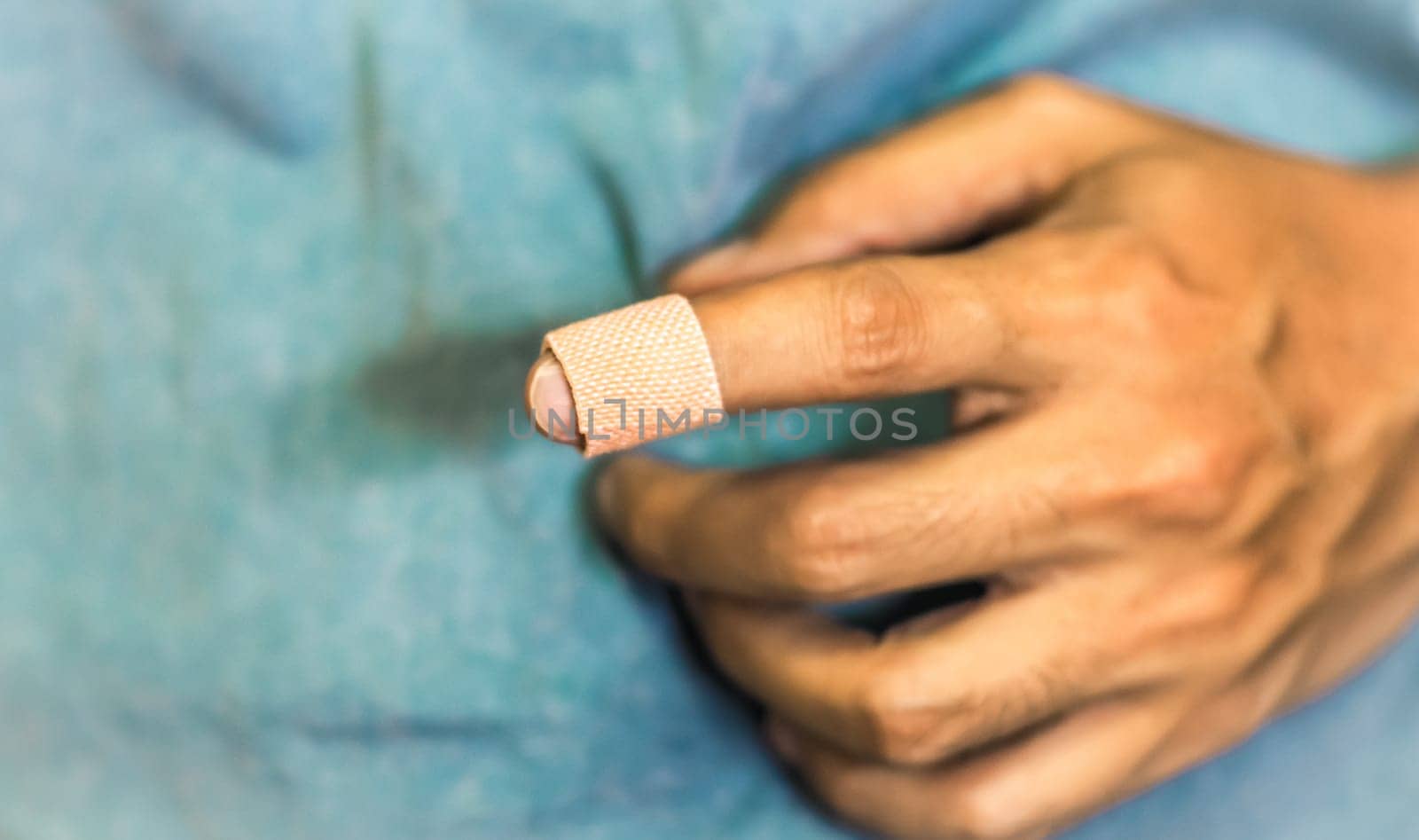 Close up of a bandage on a man's index finger against blue background. Health care first aid emergency recovery.