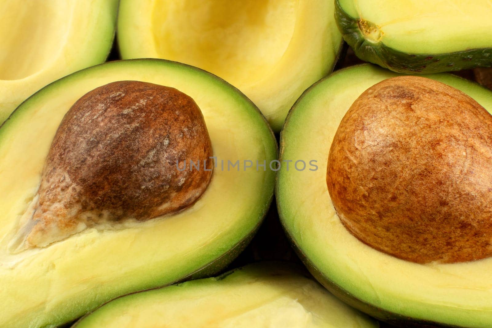 Closeup photo of avocado cut to half, brown seeds visible, with more avocados in background