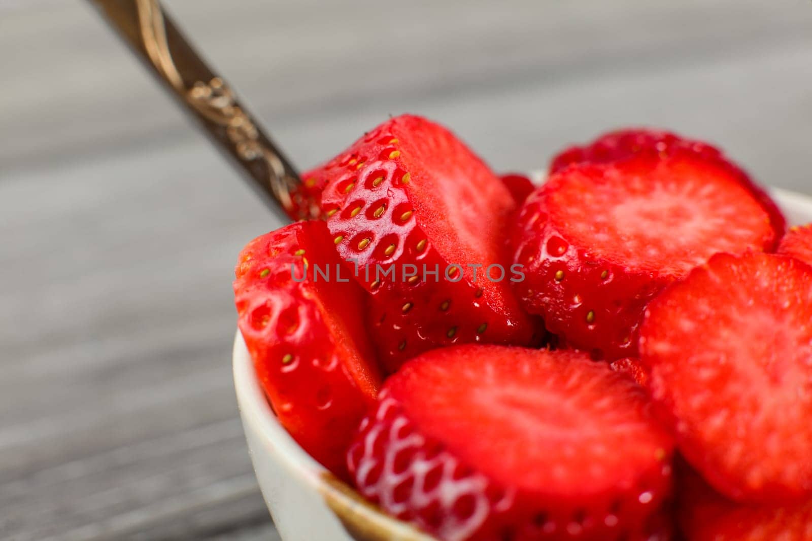 Close up - small bowl with spoon, full of strawberries cut into small circle pieces. Ready to eat healthy snack.