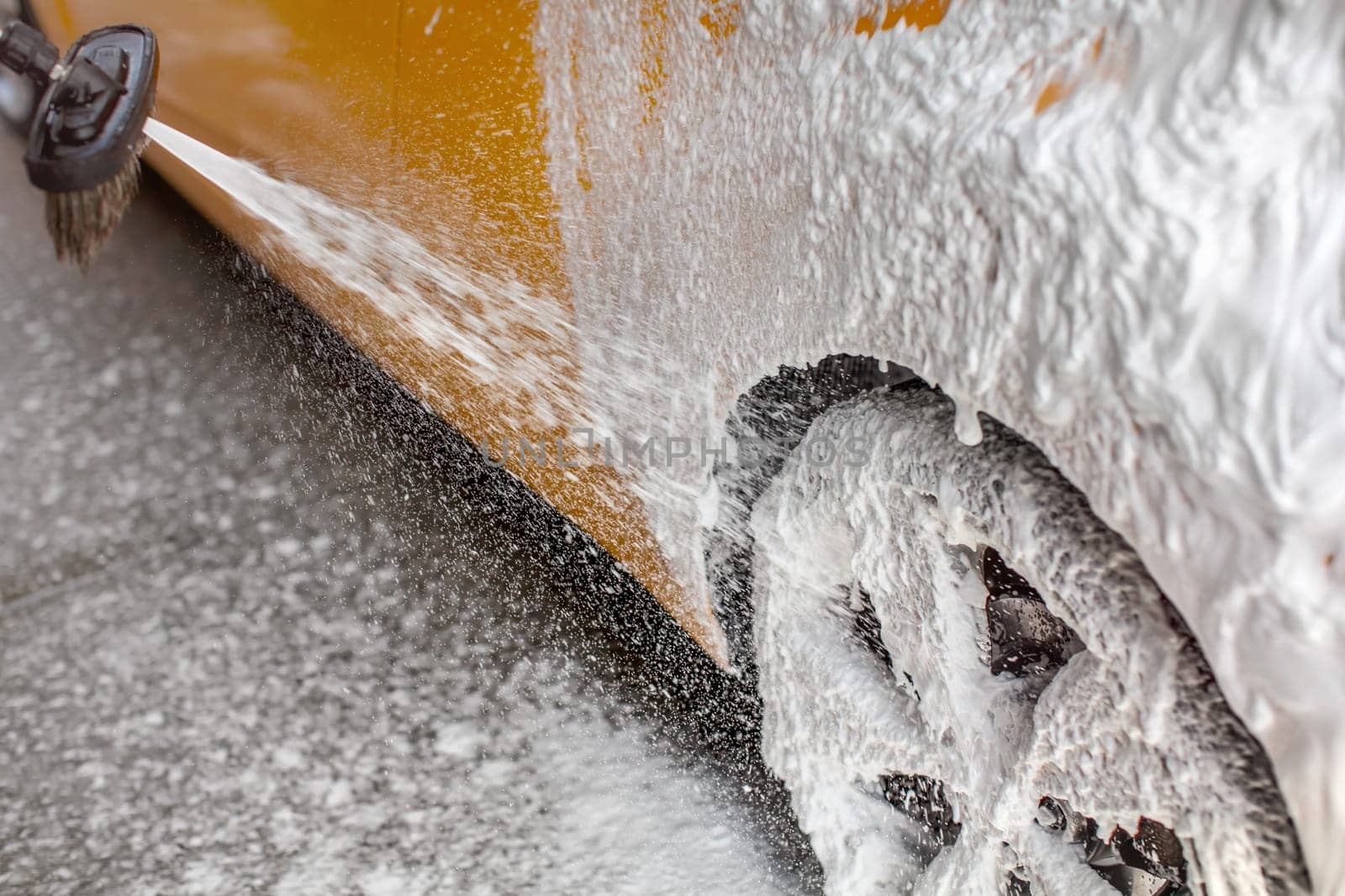 White shampoo foam sprayed on car rear wheel and side, when washed in carwash.