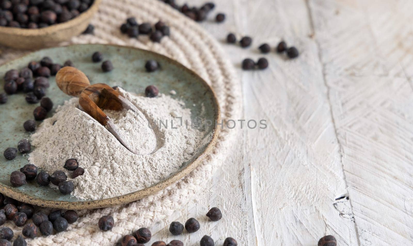 Plate and wooden scoop of black chickpea flour and beans closeup with copy space on white wooden table. Traditional beans from Apulia and Basilicata in Italy