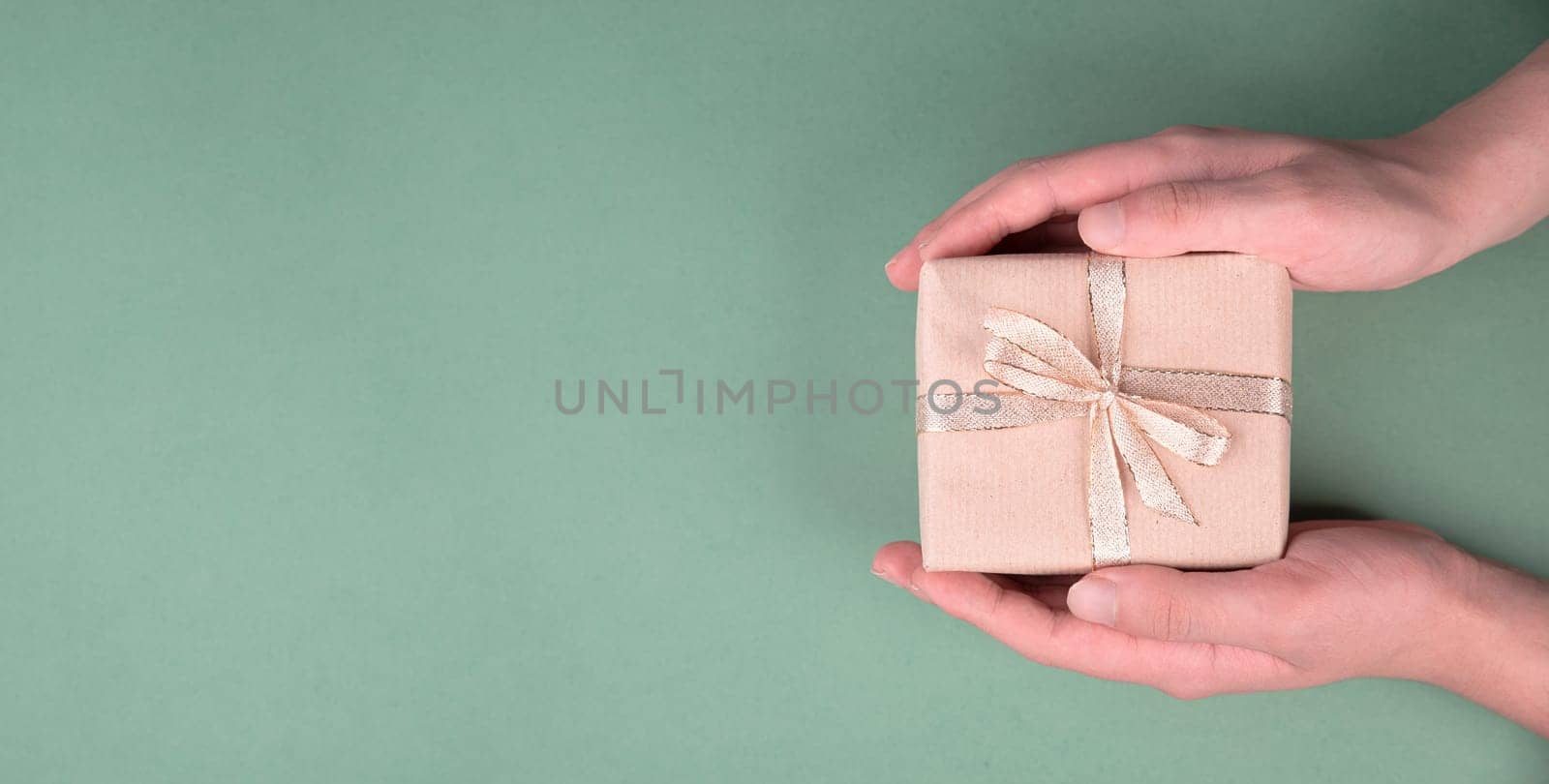 Holding a small gift box in the hands on a green colored background, holidays like birthday, fathers day, christmas, copy space for text