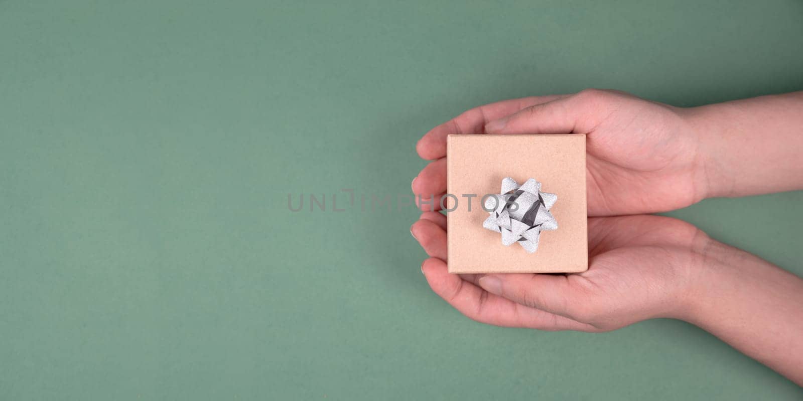 Holding a small gift box in the hands on a green colored background, holidays like birthday, fathers day, christmas, copy space for text