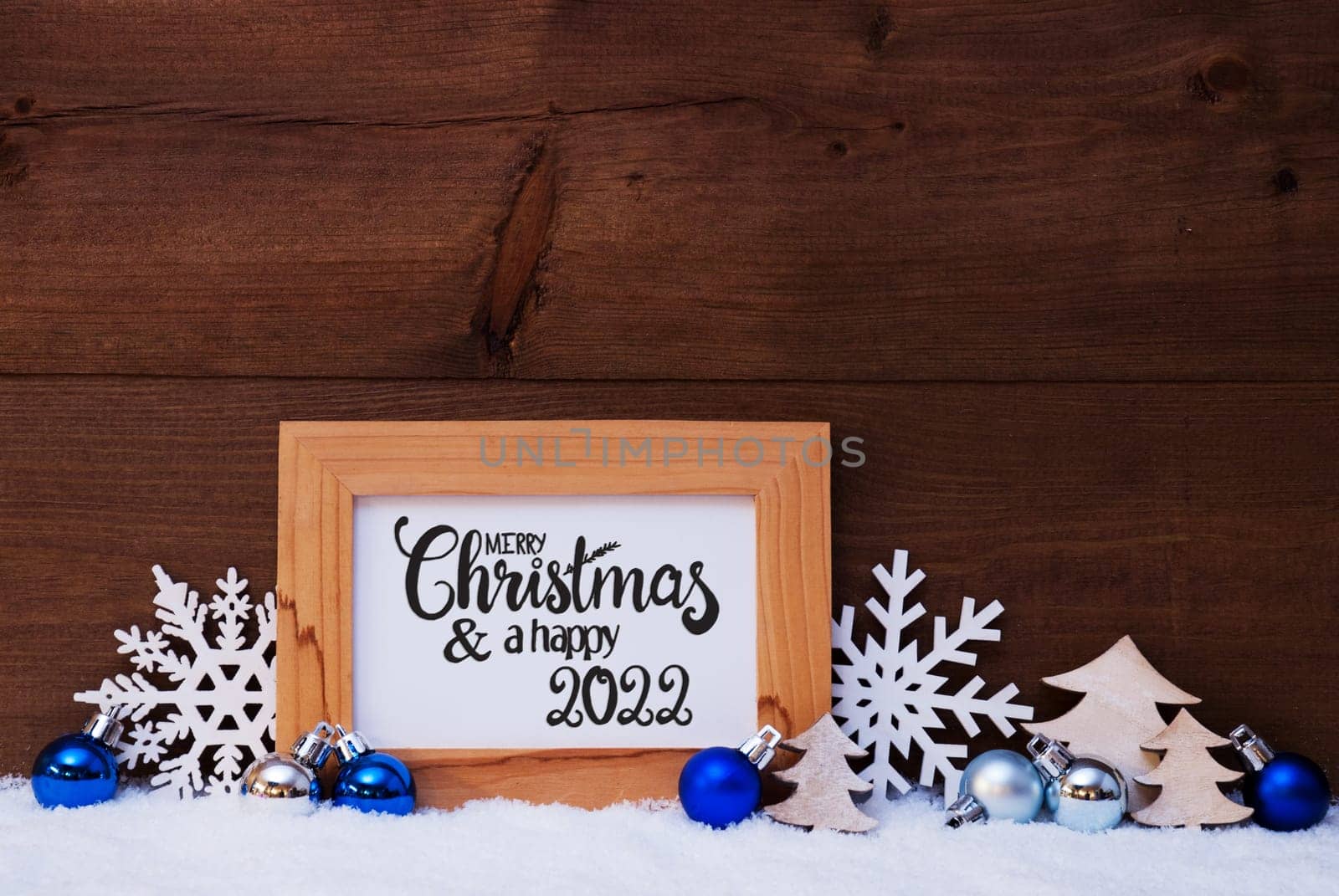 English Calligraphy Merry Christmas And Happy 2022. Blue Christmas Ornament Like Tree, Snowflake And Ball. Wooden Background With Snow