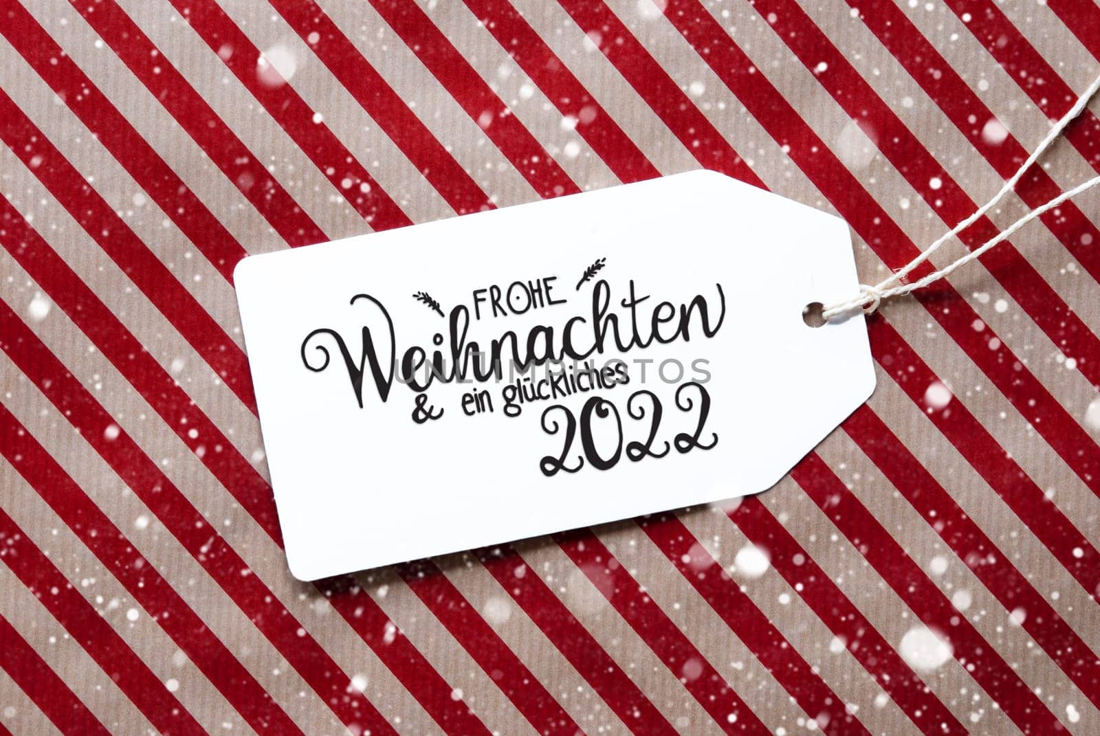 Label With German Calligraphy Frohe Weihnachten Und Ein Glueckliches 2022 Means Merry Christmas And A Happy 2022. Red Wrapping Paper As Background With Snowflakes
