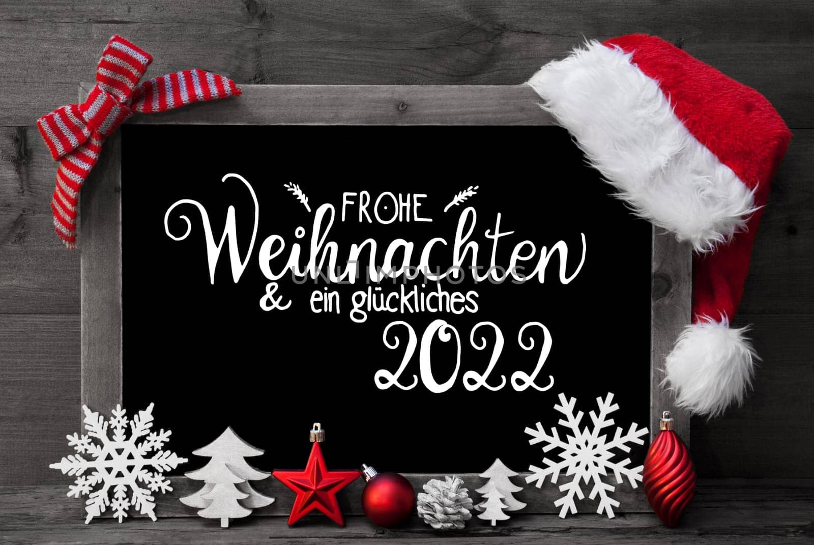 Chalkboard With German Calligraphy Frohe Weihnachten Und Ein Glueckliches 2022 Means Merry Christmas And A Happy 2022. Christmas Decoration Like Tree, Ball And Santa Hat. Gray Wooden Background