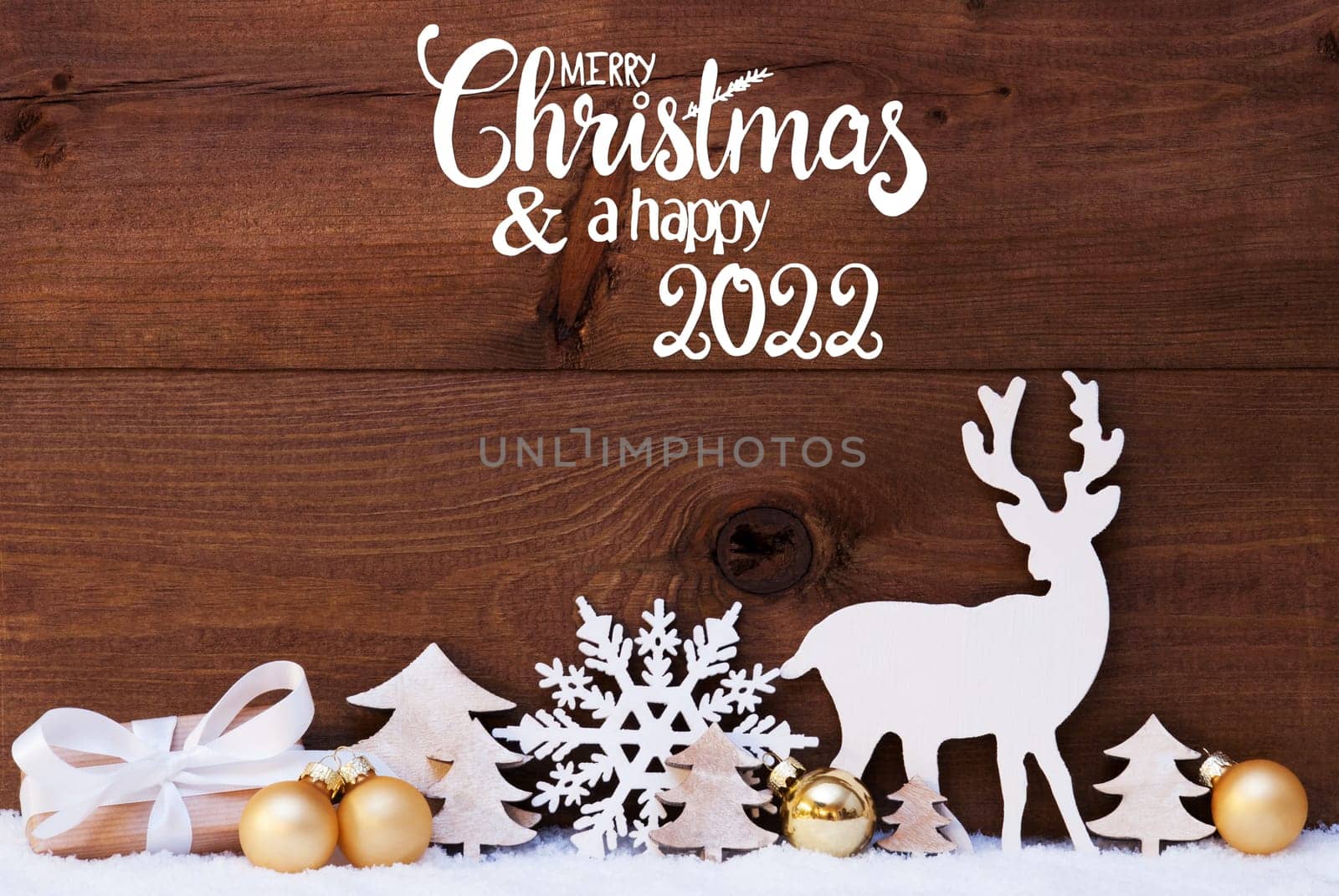 English Calligraphy Merry Christmas And A Happy 2022. Golden Christmas Decoration Like Tree, Gift, Ball And Reindeer. Wooden Background With Snow