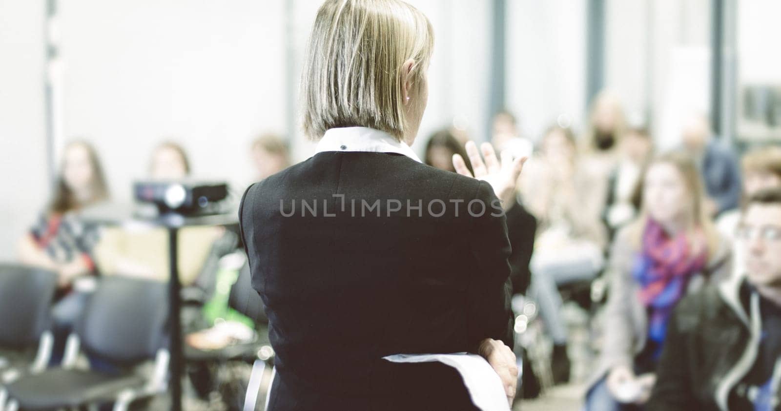 Female speaker giving a talk on corporate business conference. Unrecognizable people in audience at conference hall. Business and Entrepreneurship event.