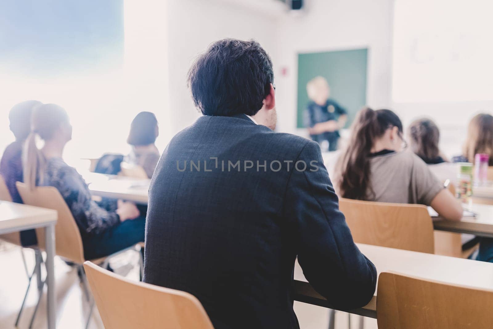 Teacher at university in front of a whiteboard screen. Students listening to lecture and making notes