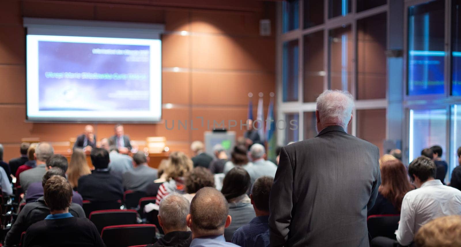 I have a question. Group of business people sitting at the chairs in conference hall. Businessman raising his arm. Conference and Presentation. Business and Entrepreneurship.