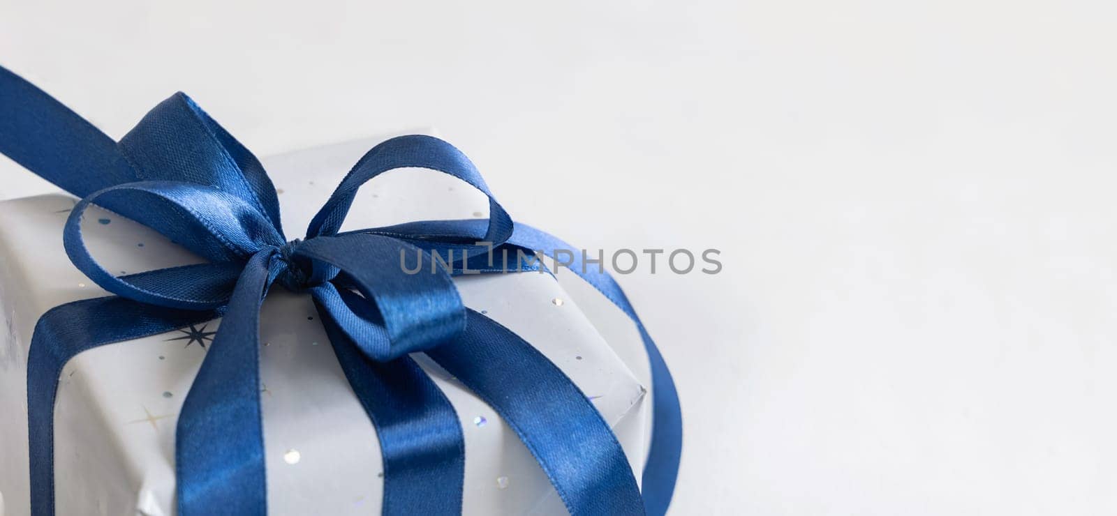 Grey Wrapped Christmas present with a blue ribbon bow on grey close up with copy space. Grey and blue winter composition with Gift box, copy space