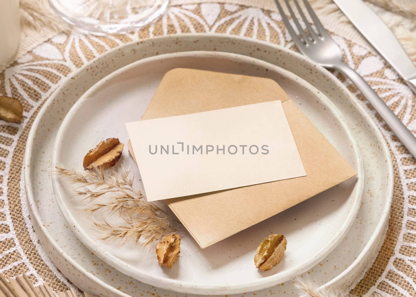 Wedding Table place with Blank card and envelope on bohemian placemat. Boho wedding card mockup. Tropical beige template with dried plants, place fot text
