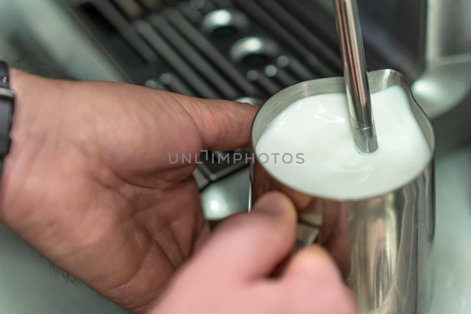 A man whisks milk for a latte in a steel jug.