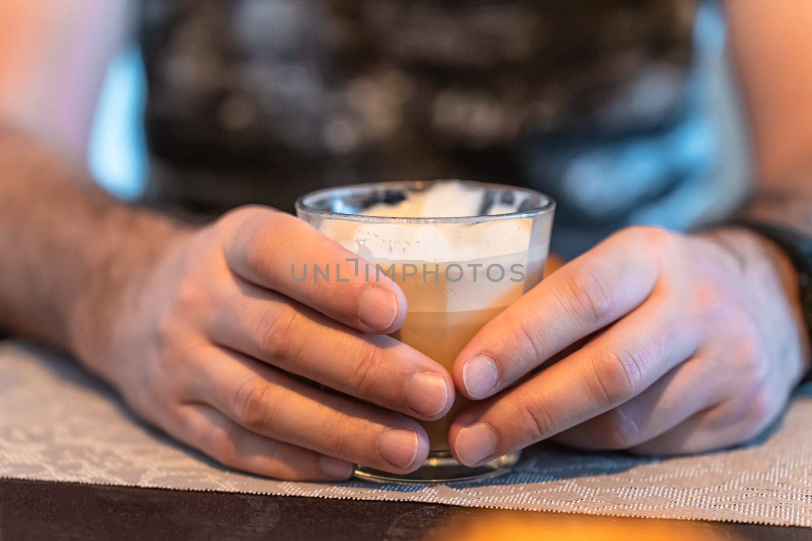 Focus in the foreground on the hands of a man who holds a glass of cappuccino