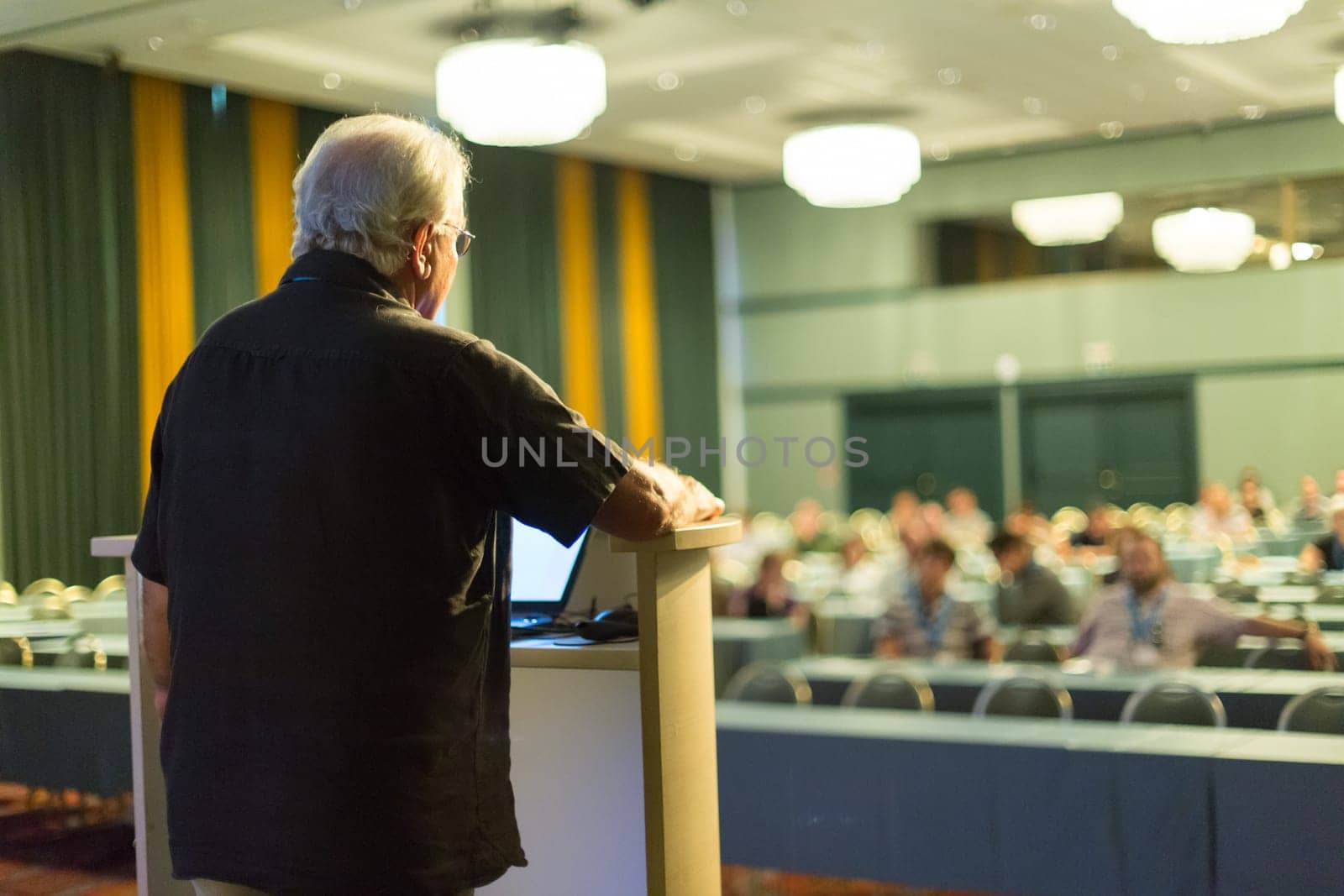 Casualy dressed senior professor giving talk at scientific conference. Audience at the conference hall. Research experts and entrepreneurship event.