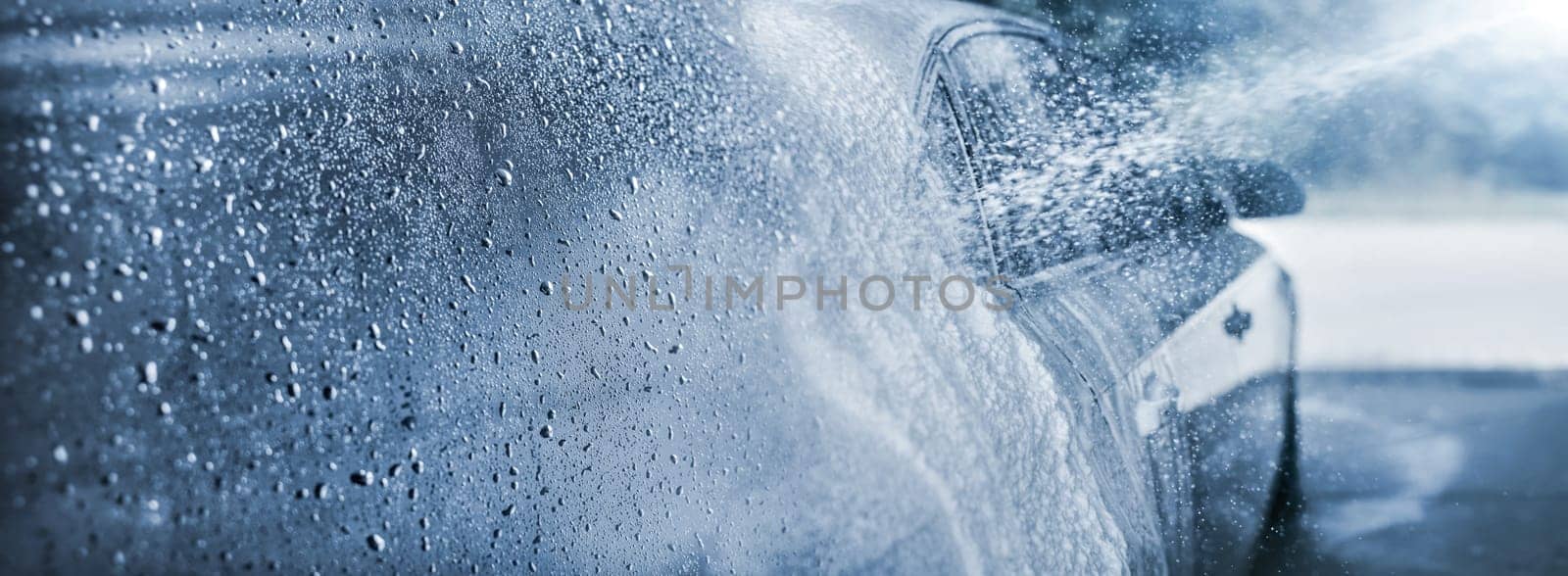Abstract carwash banner, focus only on drops of water, jet spraying to car out of focus, toned in light blue color.
