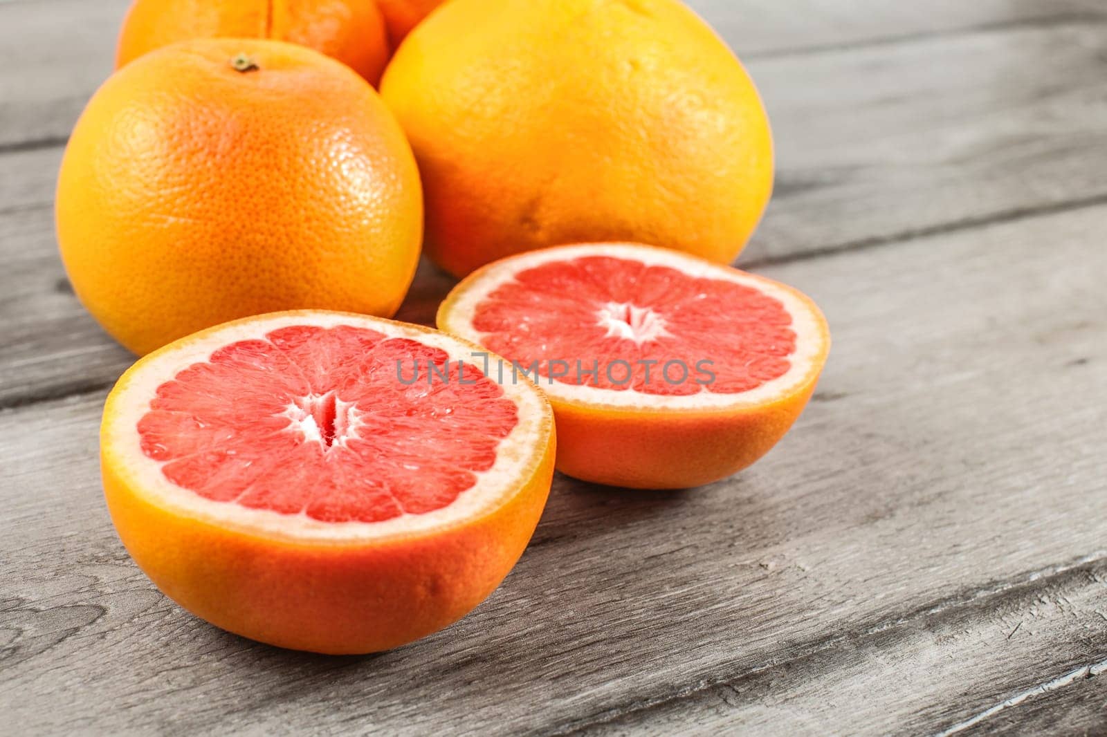 Pink red grapefruit cut in half, with more citrus in background on rustic desk.