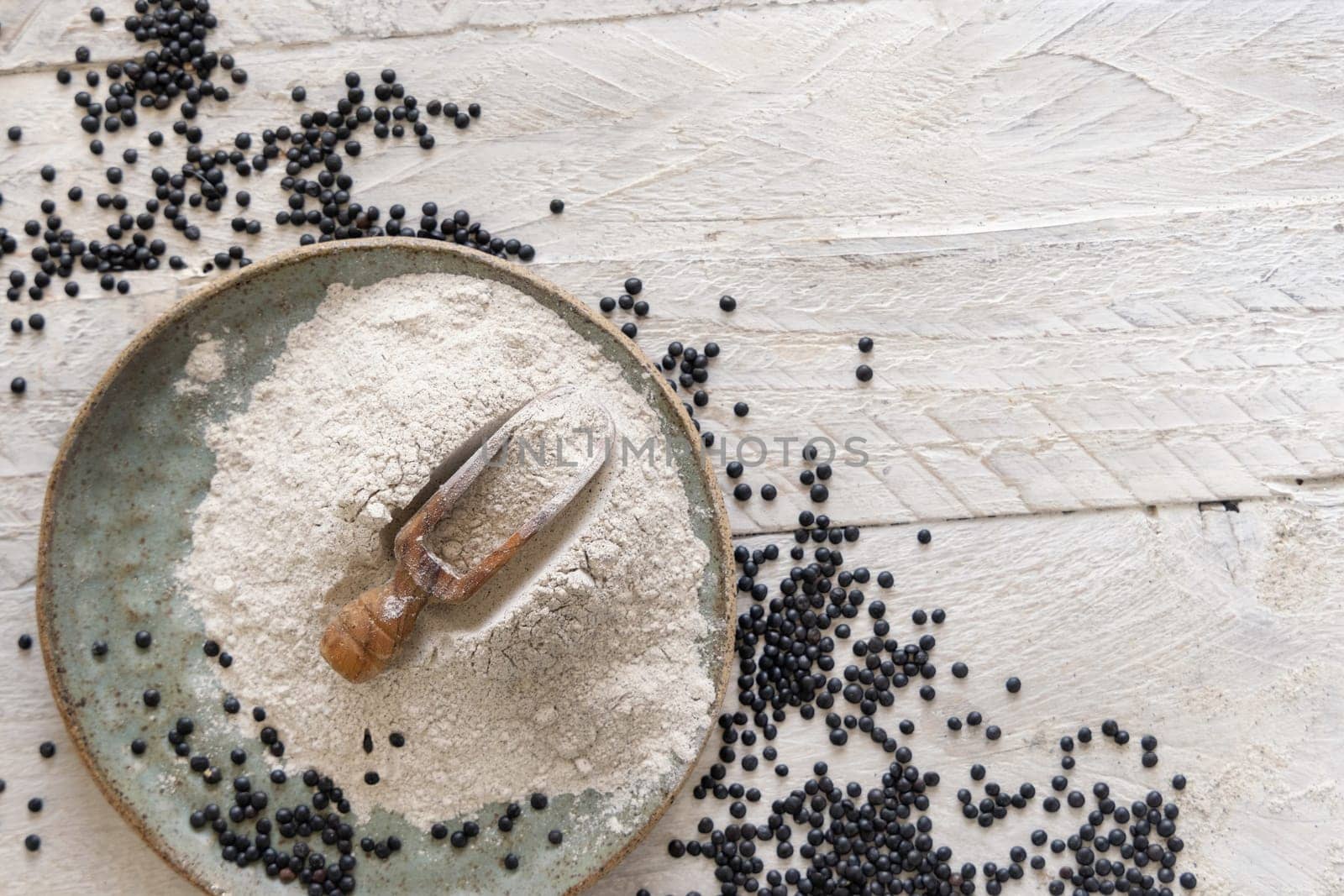 Plate with a scoop of black lentils flour and beans on white wooden table top view with copy space. Alternative flour, healthy eating, vegetarian concept. Traditional Asian and North African cuisines
