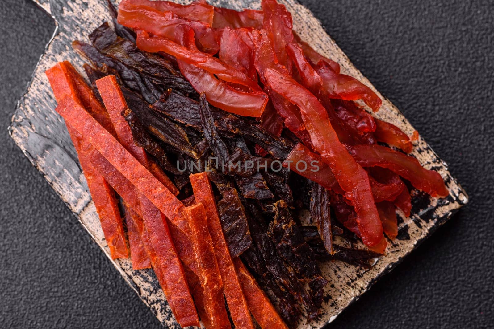 Jerky, dried fish in the form of sticks with salt, spices and herbs on a dark concrete background