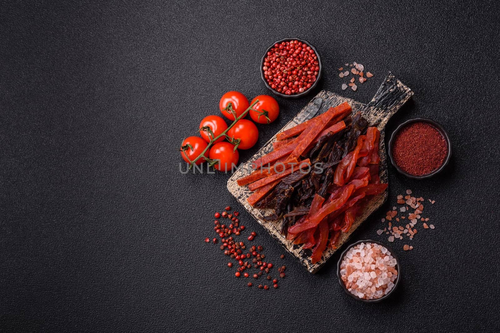 Jerky, dried fish in the form of sticks with salt, spices and herbs on a dark concrete background