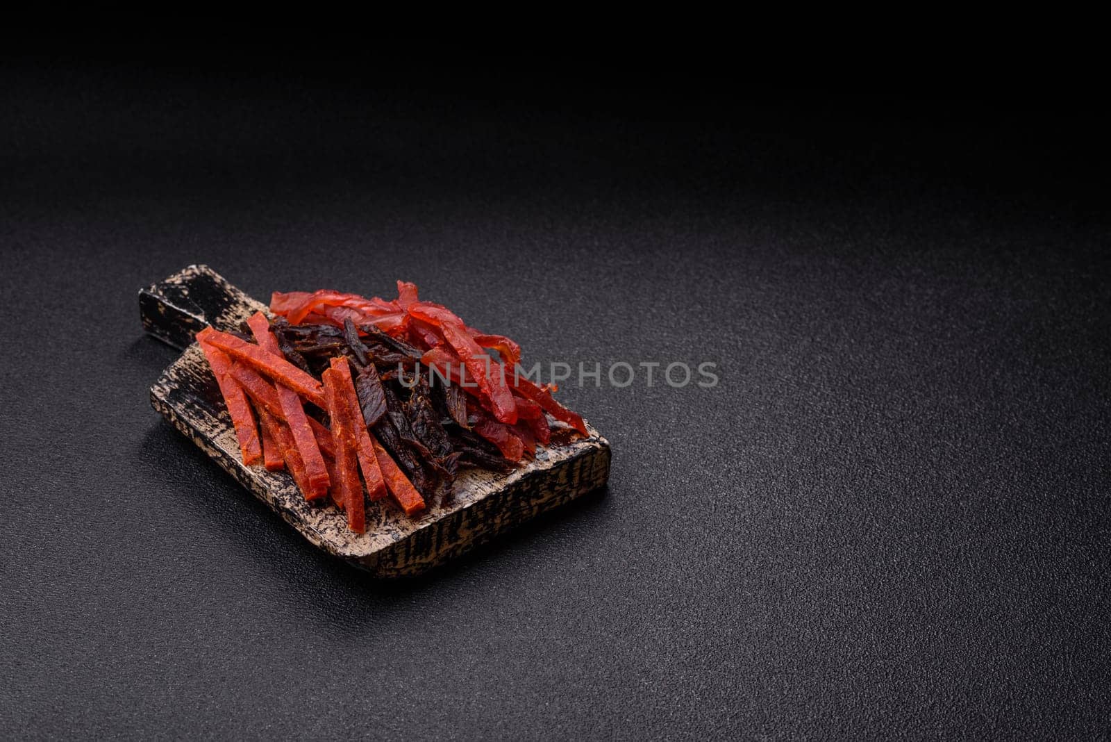 Jerky, dried fish in the form of sticks with salt, spices and herbs on a dark concrete background