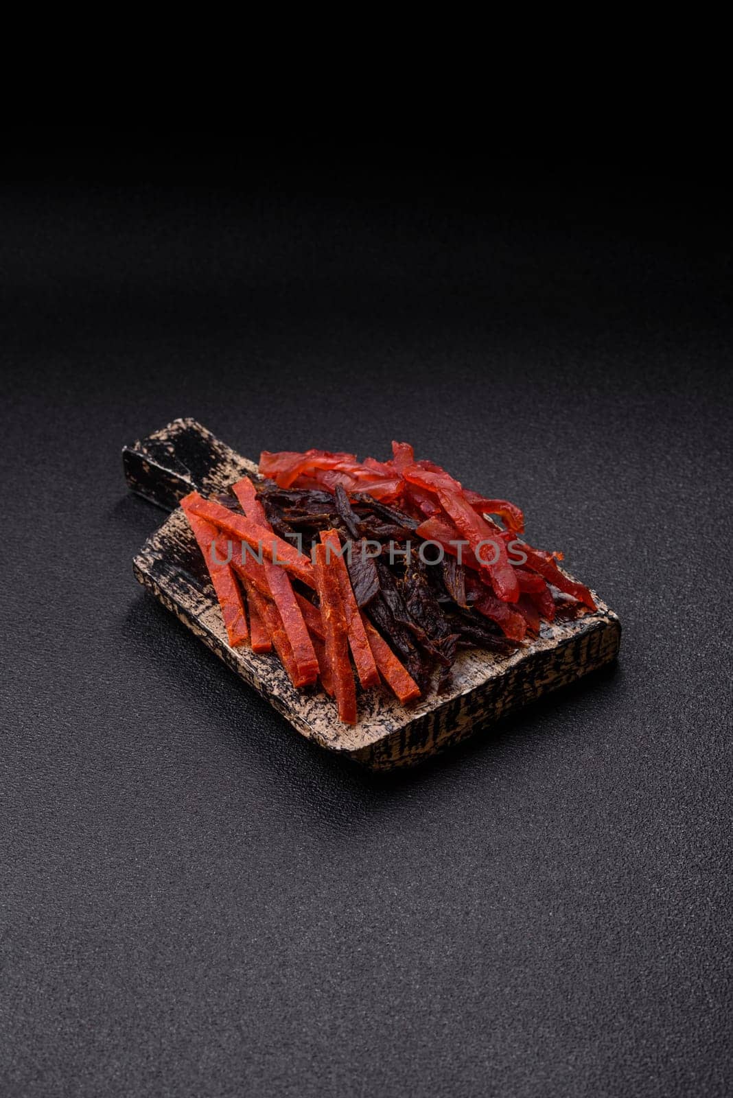 Jerky, dried fish in the form of sticks with salt, spices and herbs on a dark concrete background