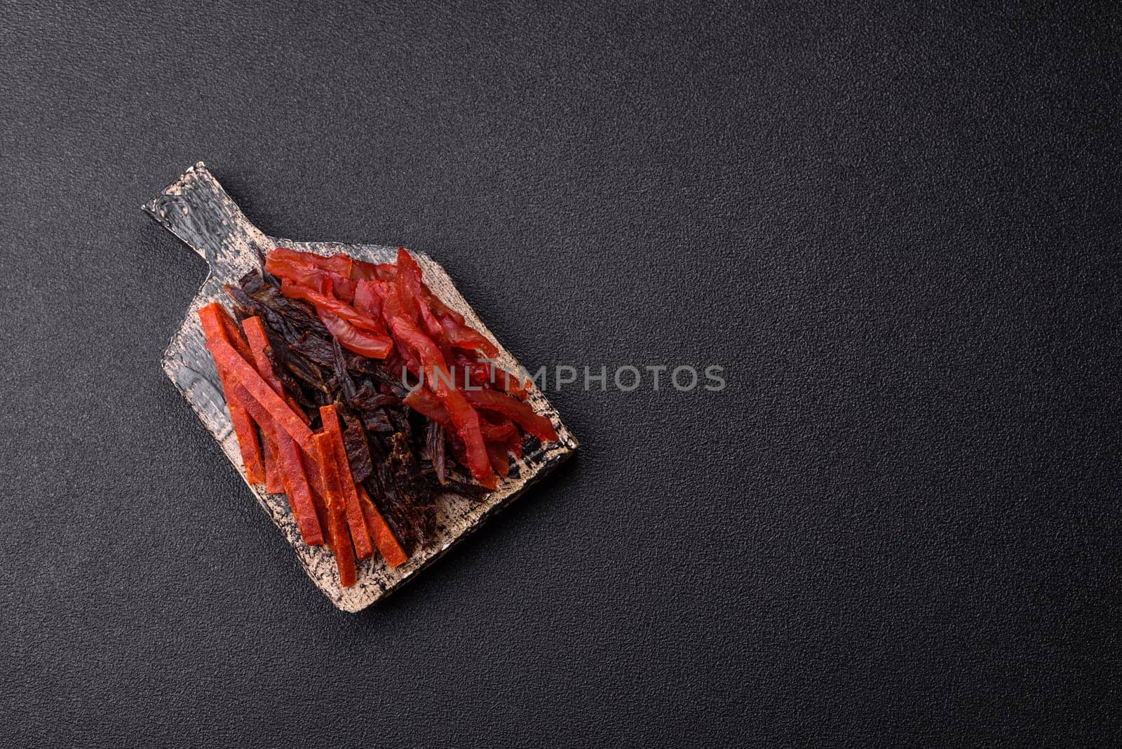 Jerky, dried fish in the form of sticks with salt, spices and herbs on a dark concrete background