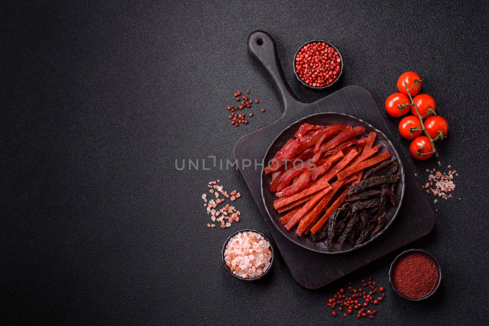 Jerky, dried fish in the form of sticks with salt, spices and herbs on a dark concrete background