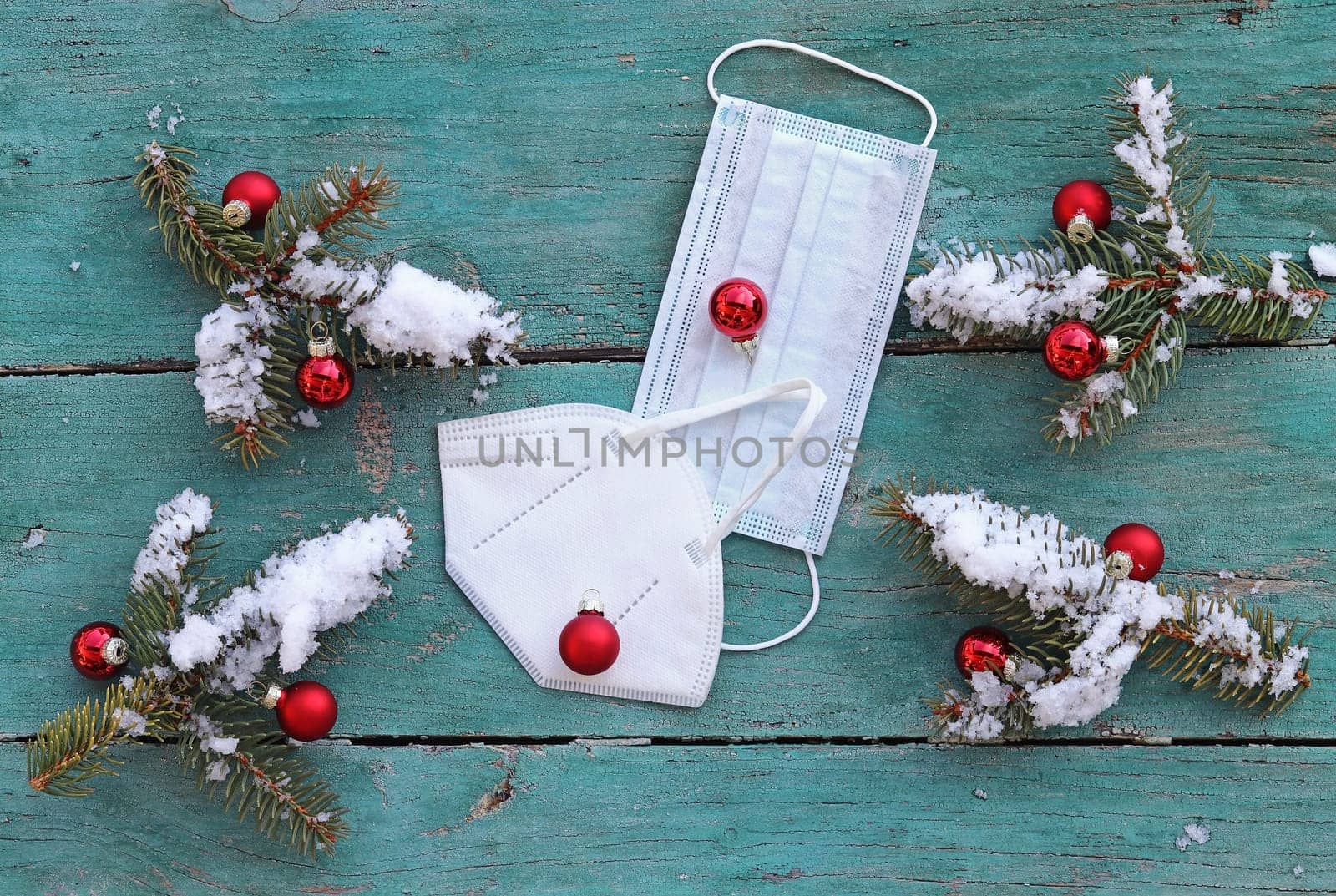 Corona and Christmas. Two protective masks next to snowy Christmas tree balls and fir branches on a blue wooden background