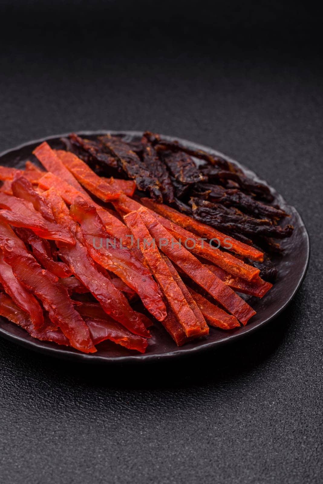 Jerky, dried fish in the form of sticks with salt, spices and herbs on a dark concrete background