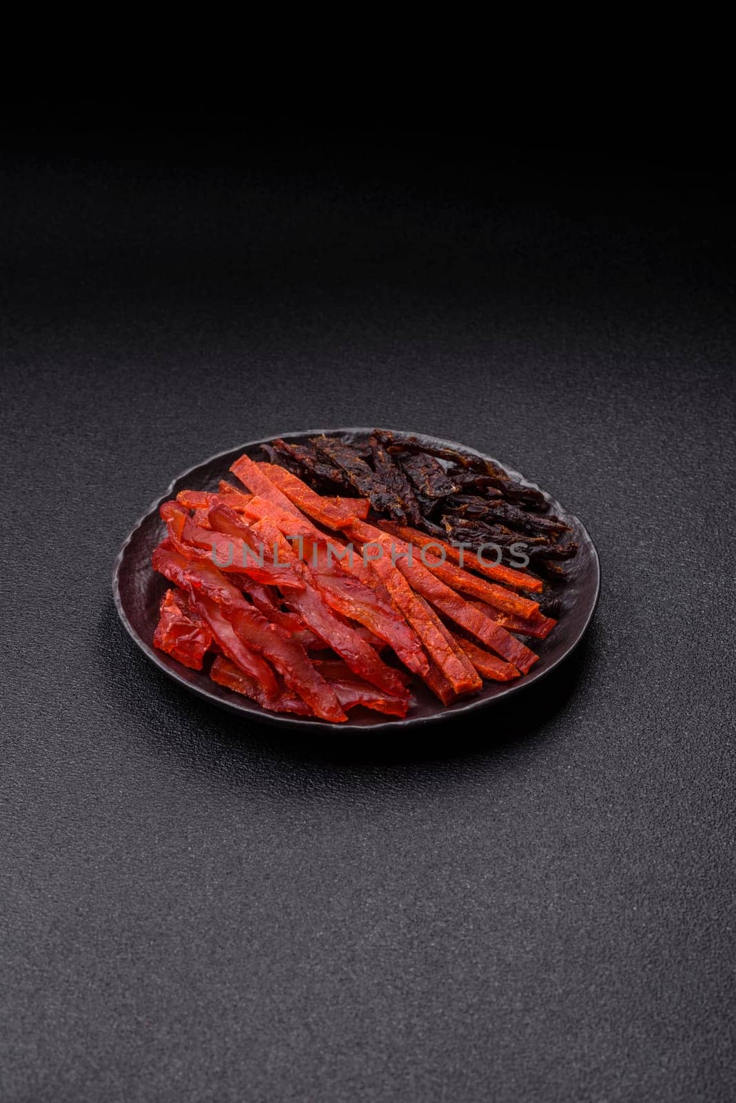 Jerky, dried fish in the form of sticks with salt, spices and herbs on a dark concrete background