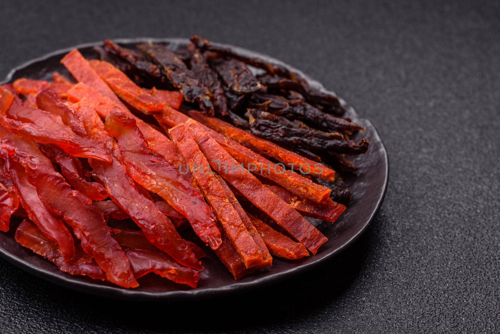 Jerky, dried fish in the form of sticks with salt, spices and herbs on a dark concrete background