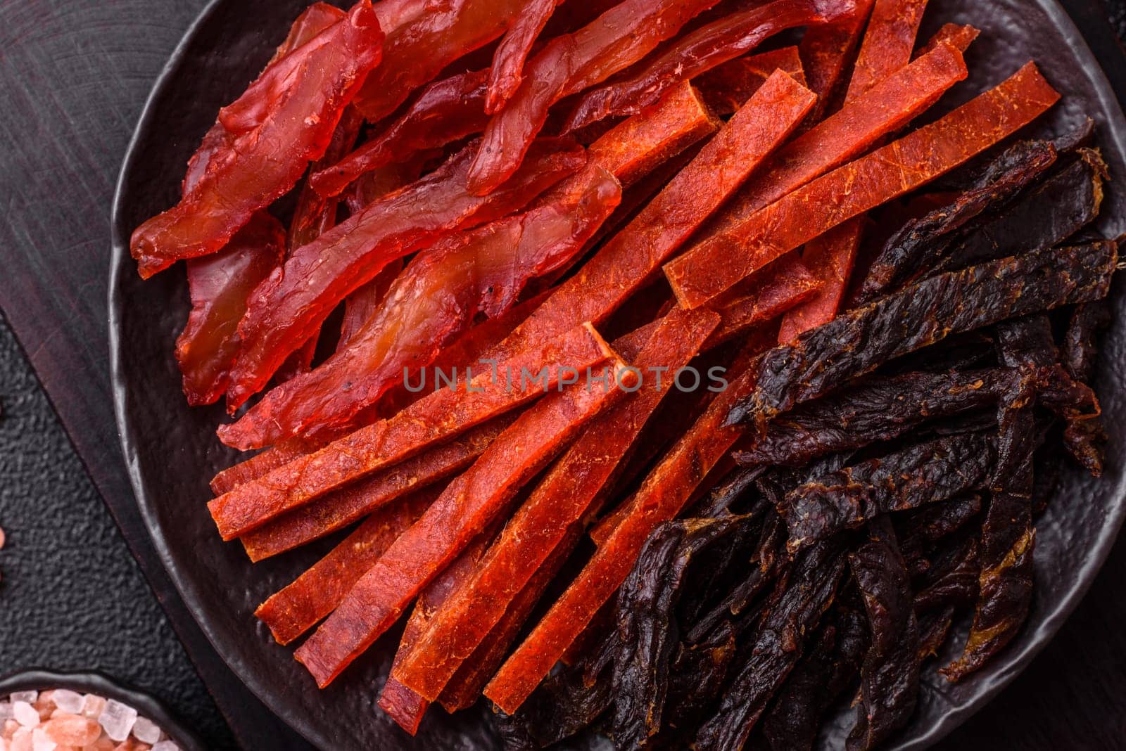 Jerky, dried fish in the form of sticks with salt, spices and herbs on a dark concrete background