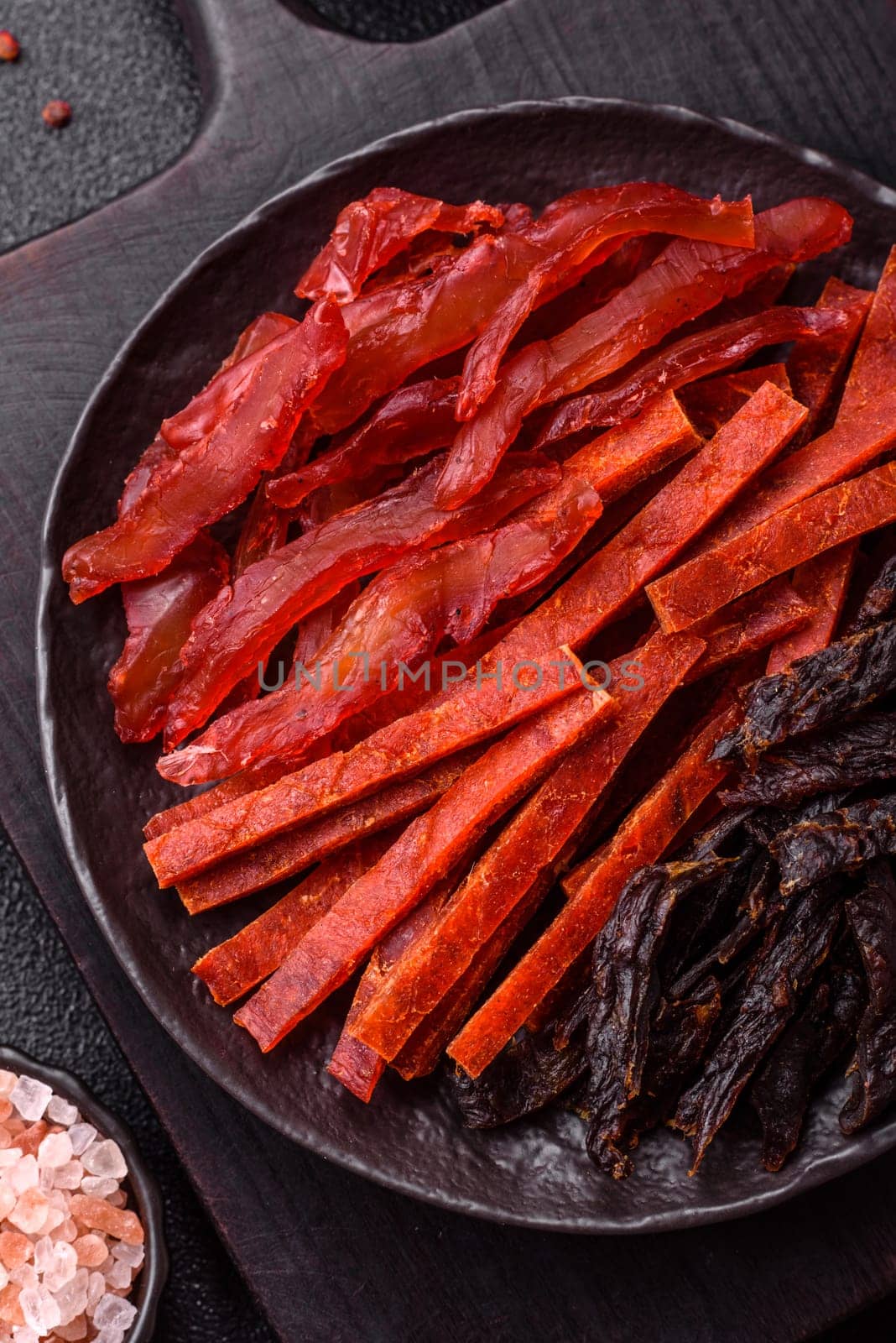 Jerky, dried fish in the form of sticks with salt, spices and herbs on a dark concrete background