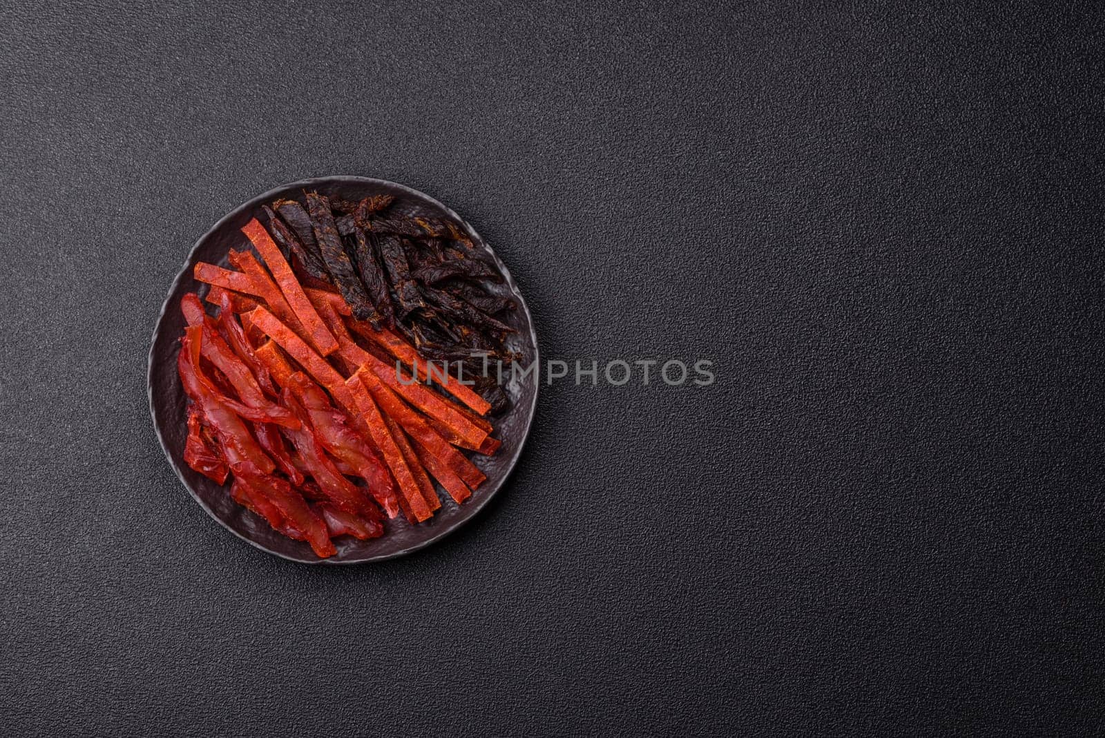 Jerky, dried fish in the form of sticks with salt, spices and herbs on a dark concrete background