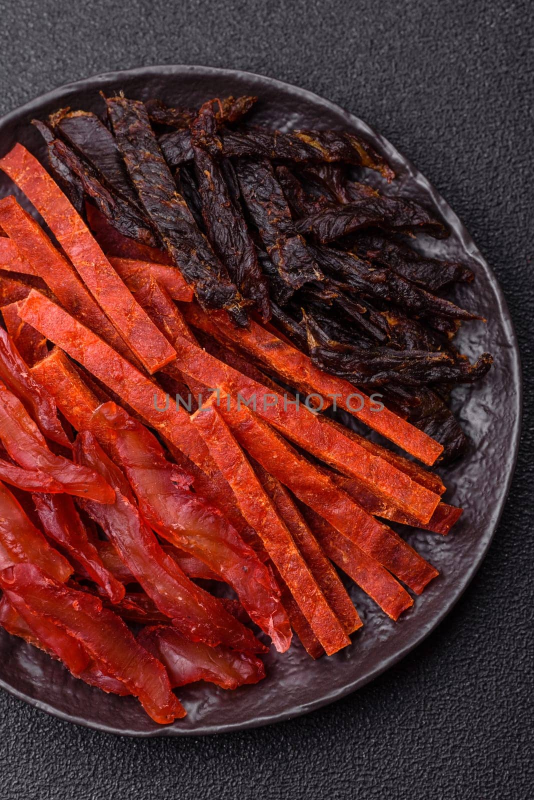 Jerky, dried fish in the form of sticks with salt, spices and herbs on a dark concrete background