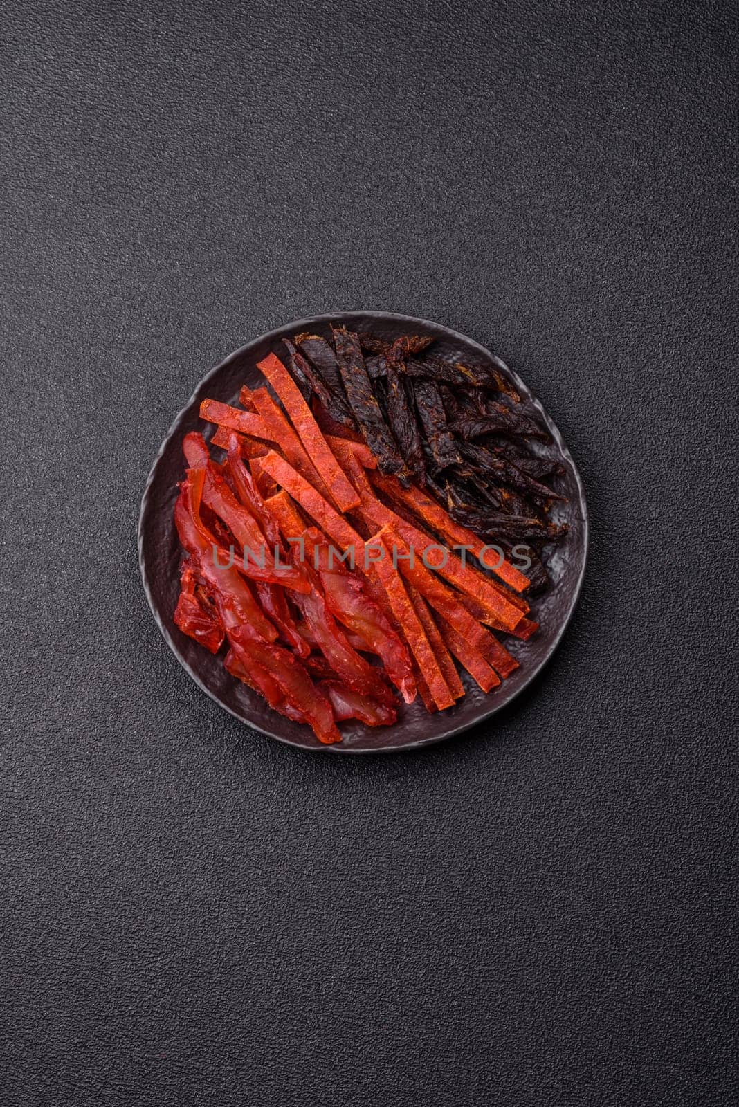 Jerky, dried fish in the form of sticks with salt, spices and herbs on a dark concrete background
