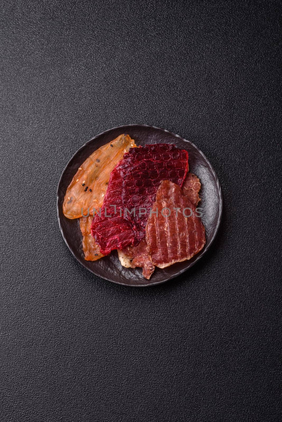 Jerky, dried meat in the form of slices with salt, spices and herbs on a dark concrete background