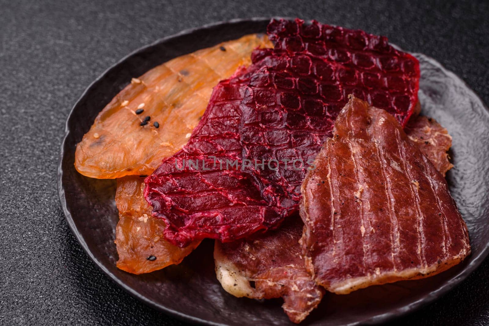 Jerky, dried meat in the form of slices with salt, spices and herbs on a dark concrete background