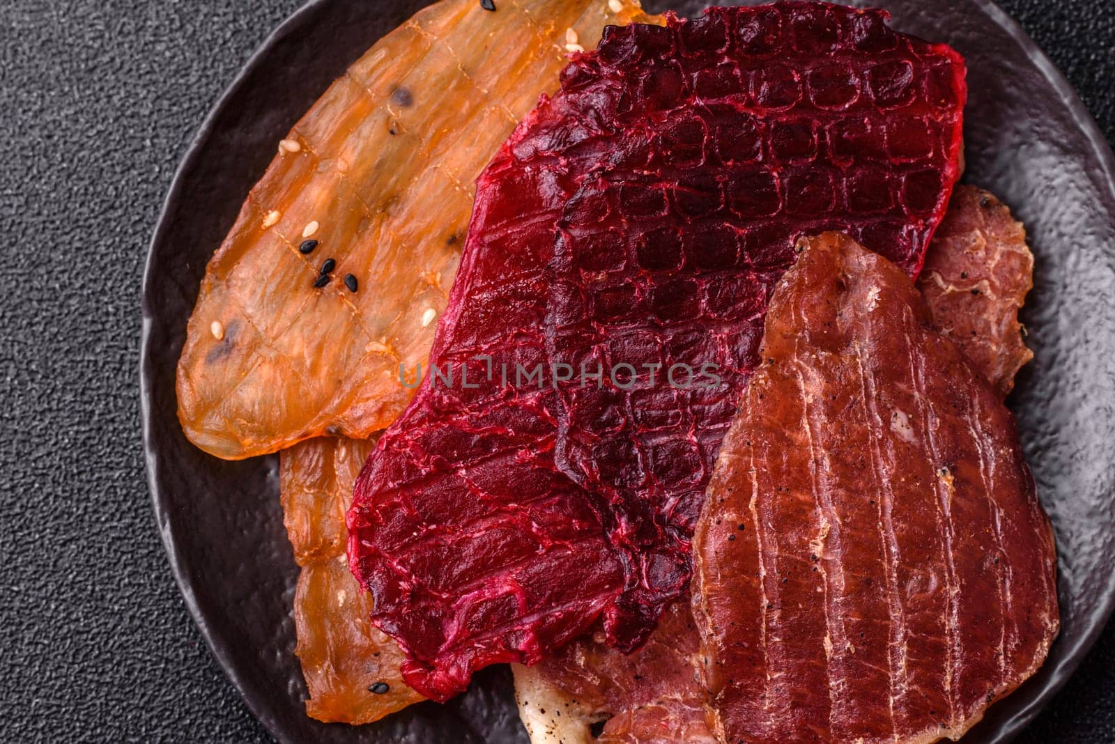 Jerky, dried meat in the form of slices with salt, spices and herbs on a dark concrete background