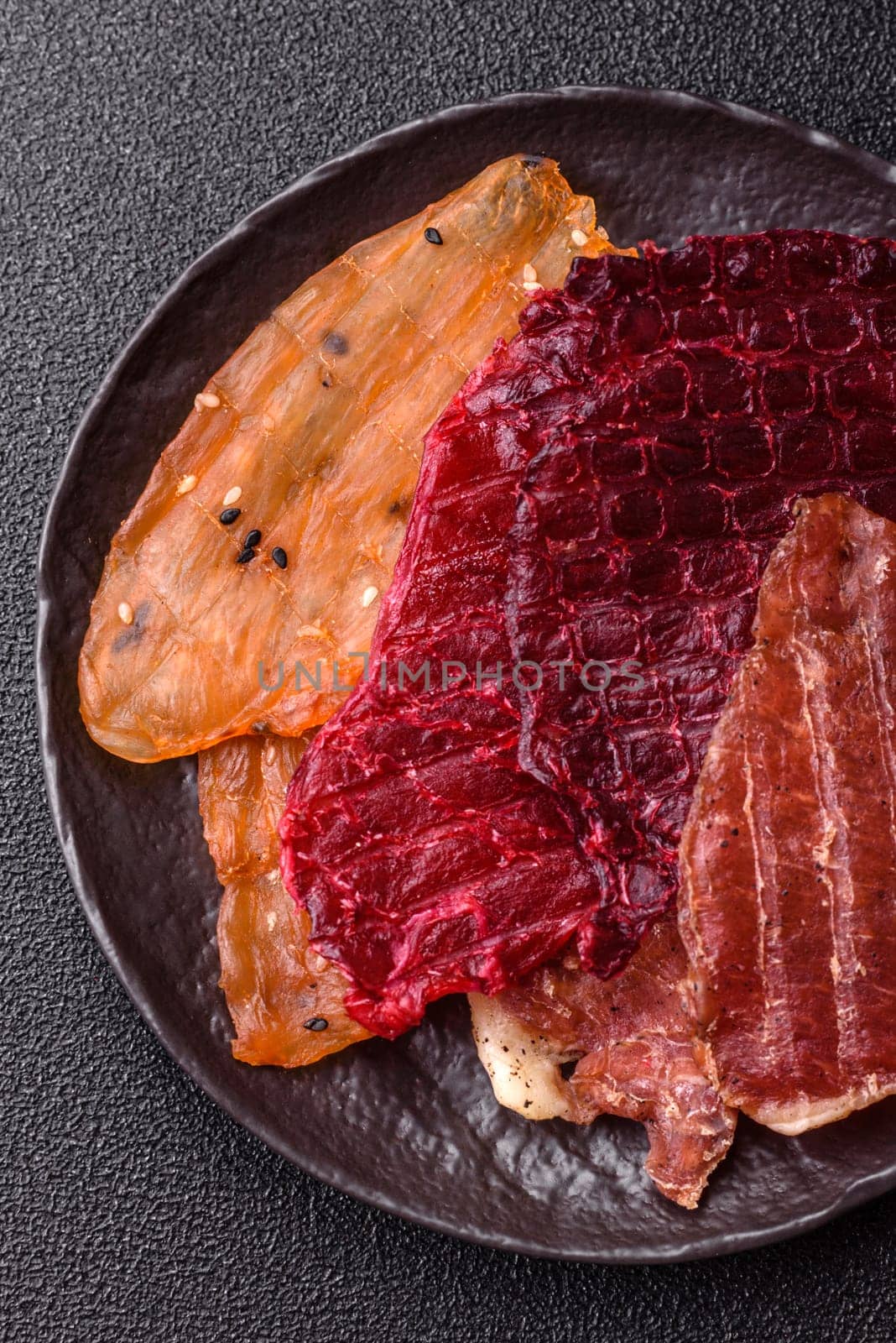 Jerky, dried meat in the form of slices with salt, spices and herbs on a dark concrete background