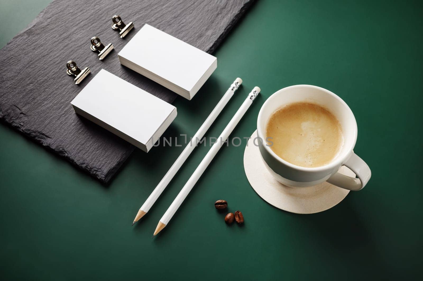 Blank stationery and coffee cup on green background.
