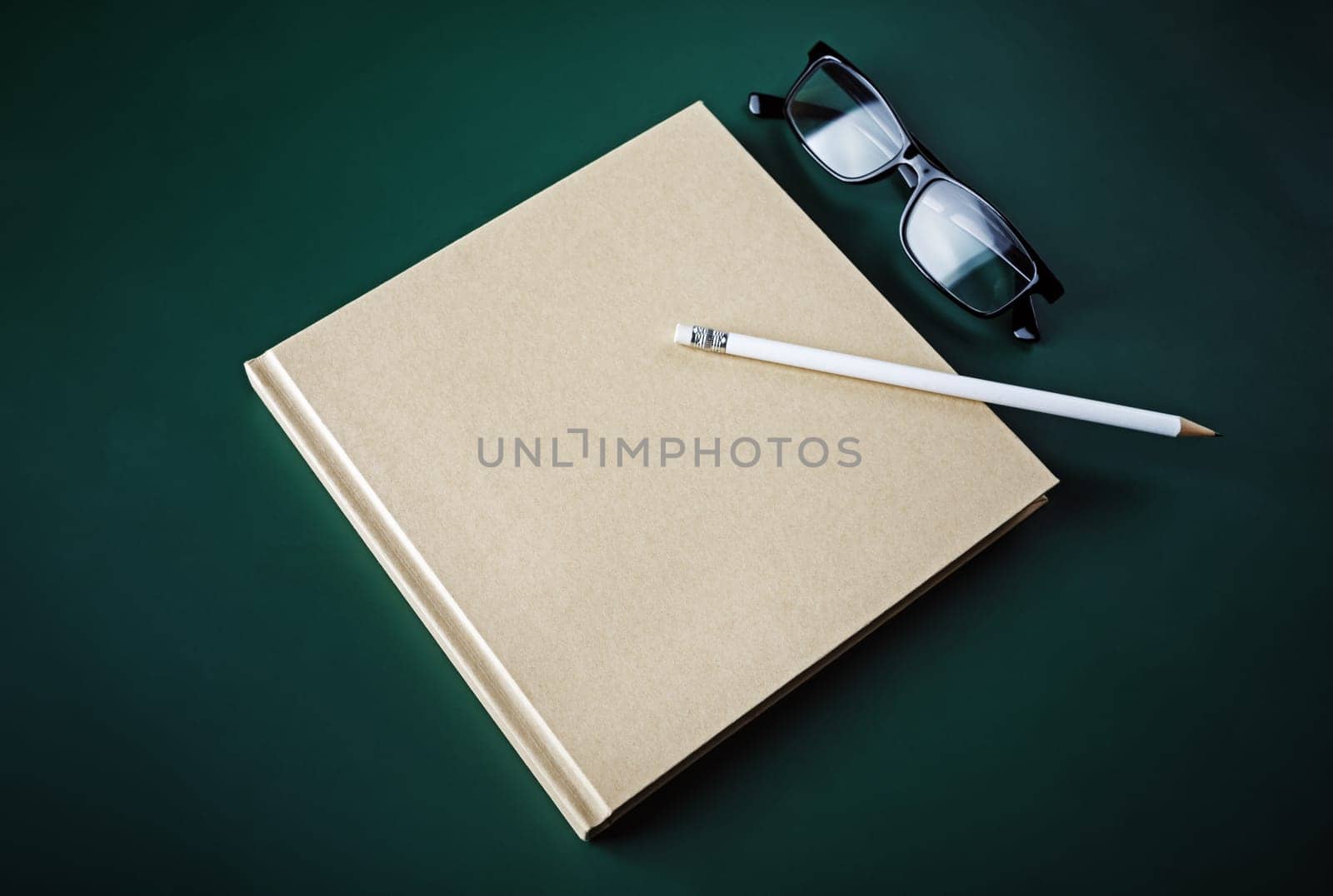 Blank closed book, pencil and glasses on green background.
