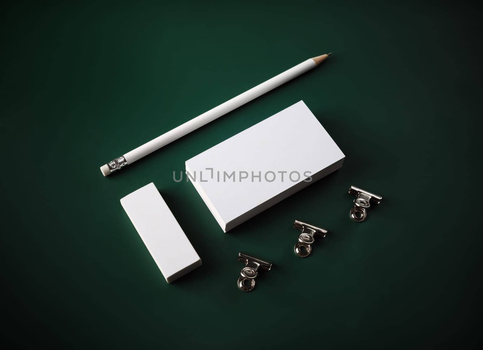 Photo of blank stationery. Blank business card, pencil, eraser and clips on green background.