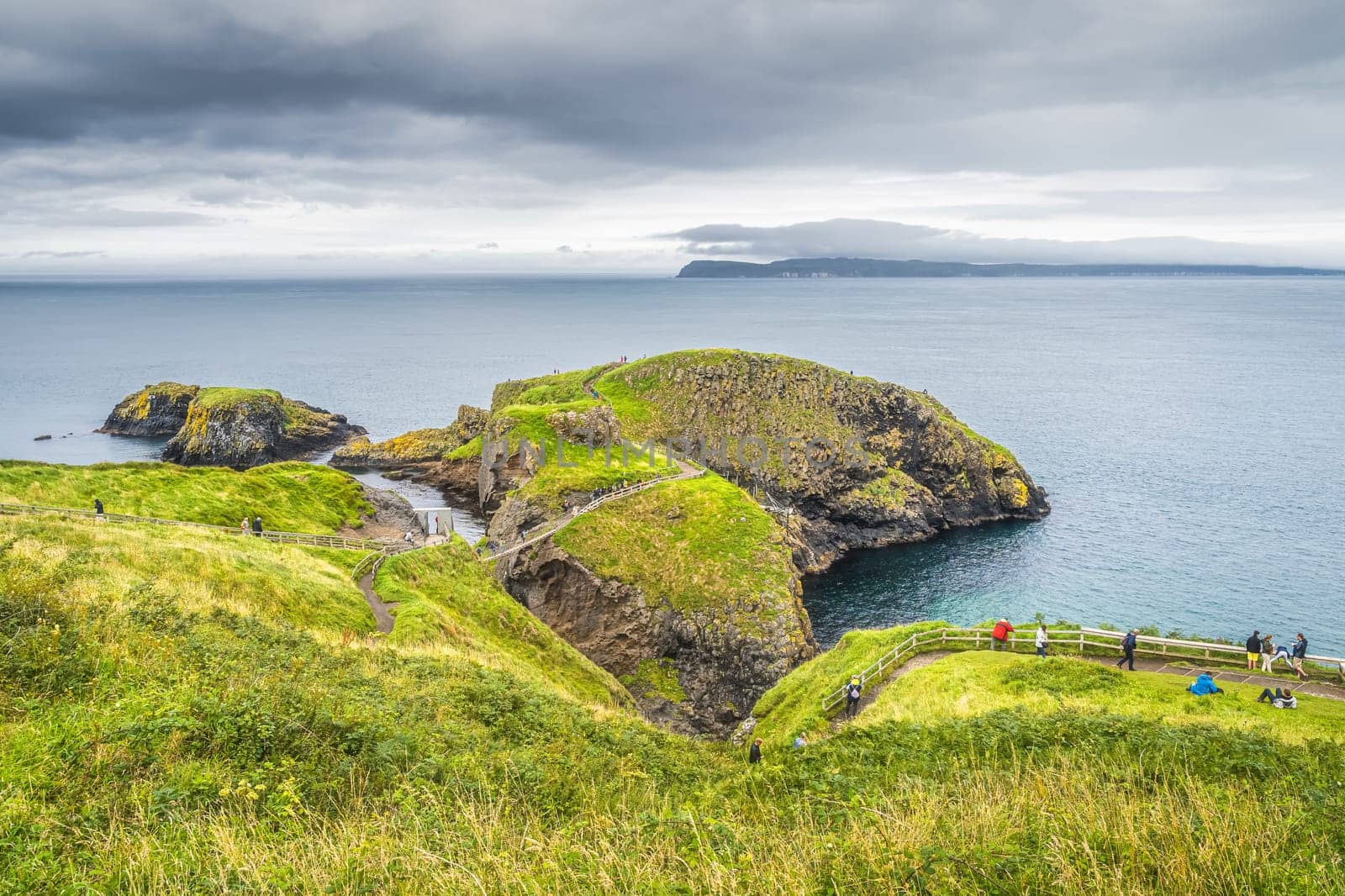 Tourists sightseeing the Carrick a Rede rope bridge and scenic island surrounded by turquoise Atlantic Ocean, Wild Atlantic Way, Northern Ireland