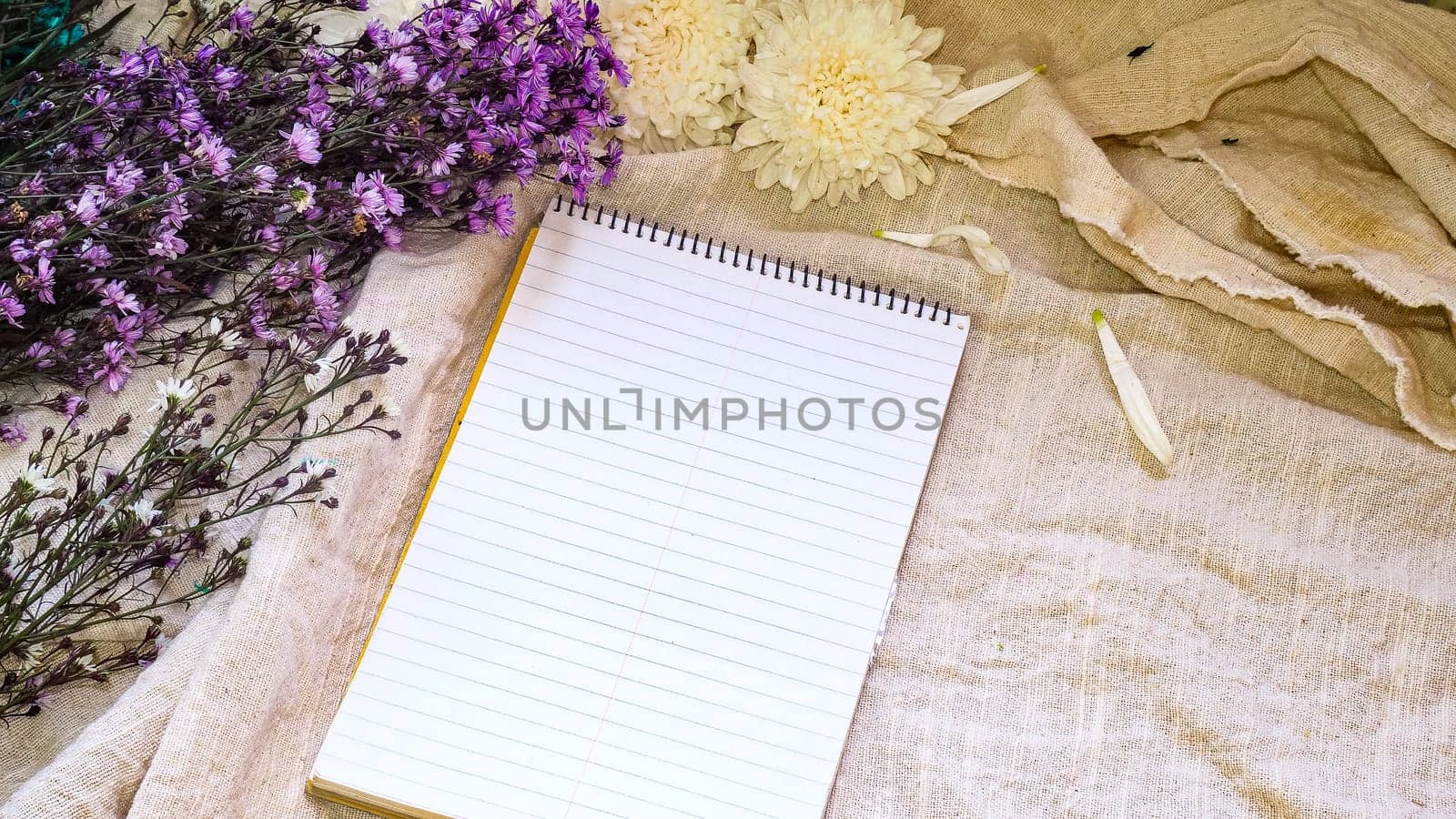 Blank paper and flower decoration. Greeting card on a white natural  linen background. Top view. Copy space.