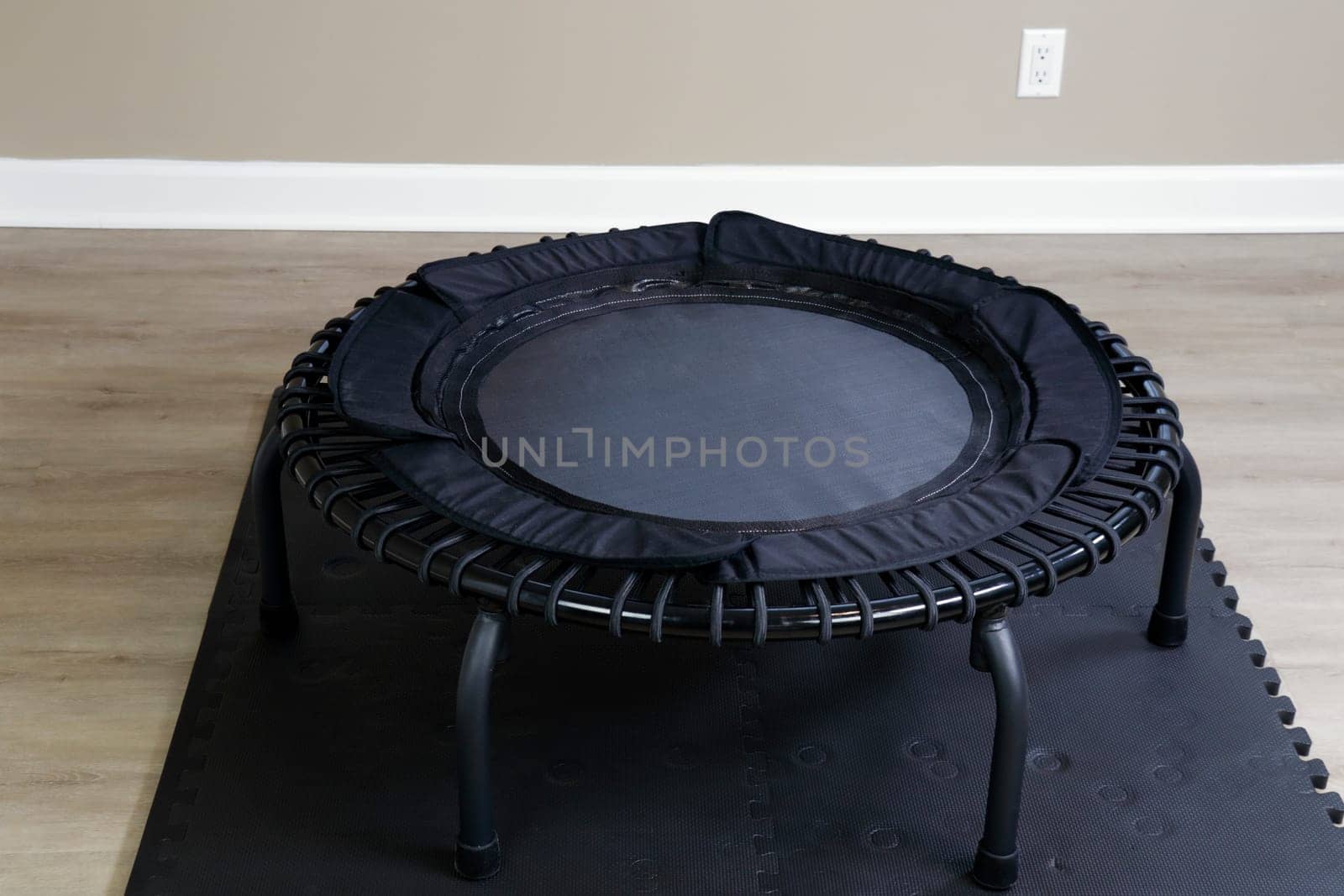 Bungee rebounder on a black exercise mat on vinyl plank simulated wood grain brown and beige flooring. Healthy bungee rebounding exercise equipment on a thick exercise mat in indoor space in the day..
